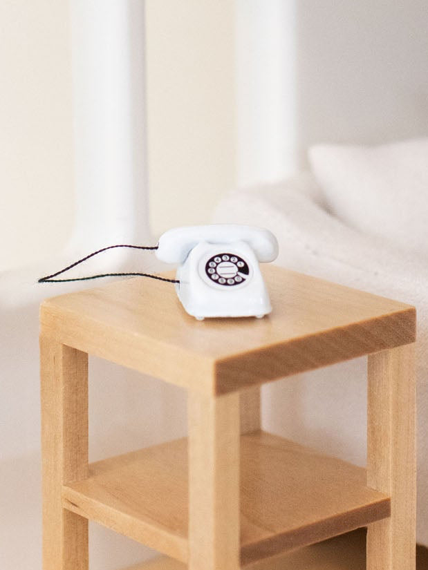 White phone on a wooden side table next to a white sofa with a white rug.